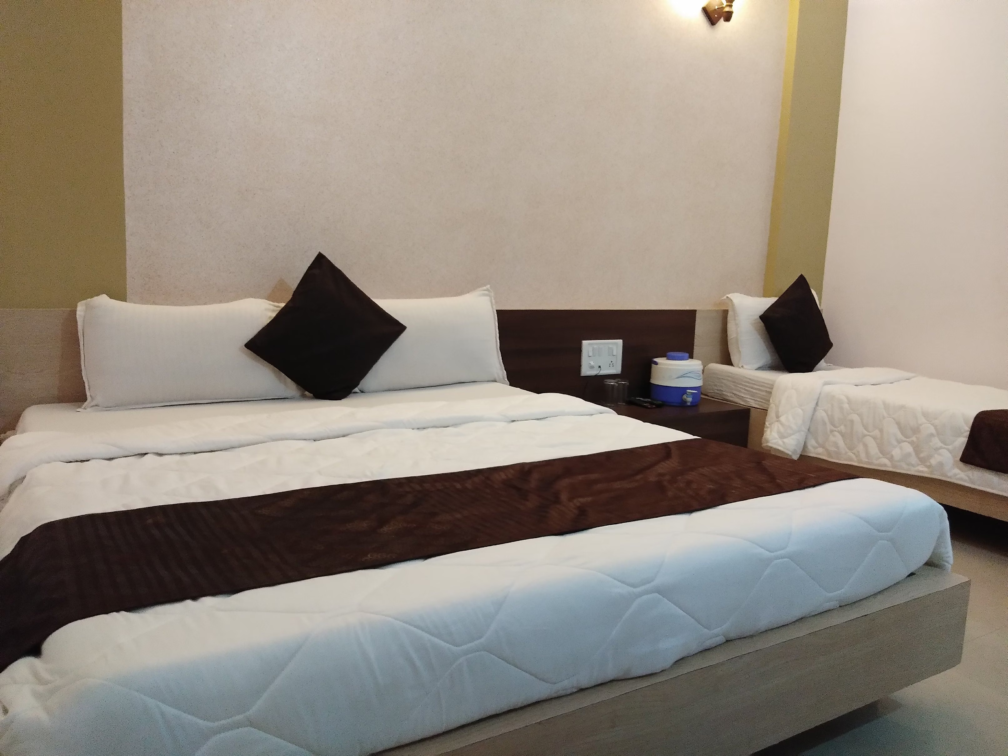 Hotel Somnath Atithigruh triple room with seating area and window, providing a relaxing space for guests.